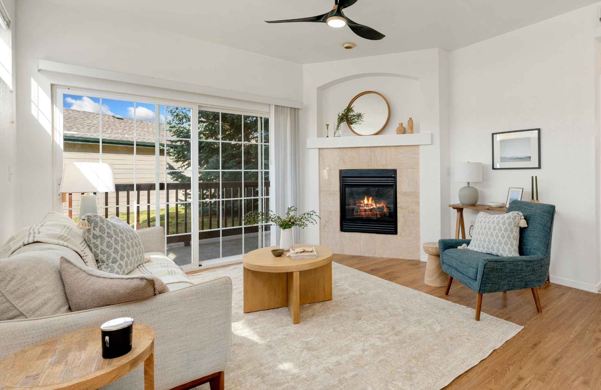 rooted-interior-design-eastborough-ks-custom-home-design-living-room-with-large-window-wood-floors-corner-fireplace-with-round-mirror-curated-millwork